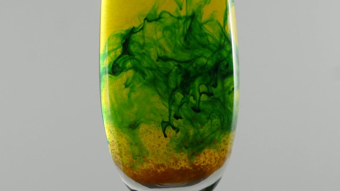 绿色的液体在水中形成形状，杯子里有橙色的颗粒