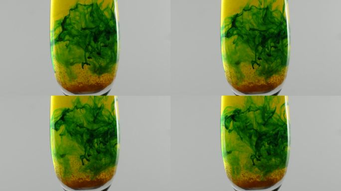 绿色的液体在水中形成形状，杯子里有橙色的颗粒