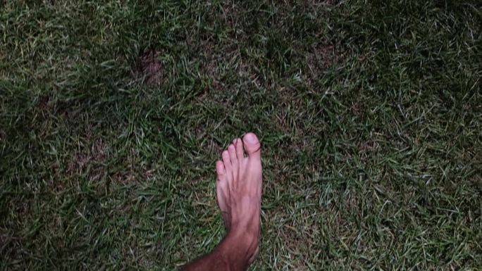 男子光着脚走在乡间的绿草地上，特写4k电影慢动作