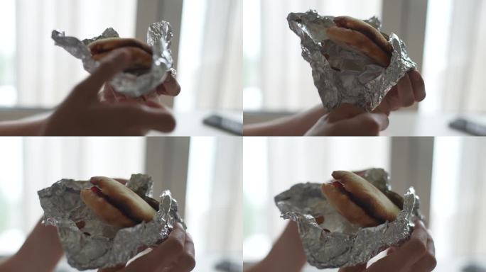 特写镜头中，一个无法辨认的人用手用锡箔纸打开美味的热三明治。男性手臂握着，打开，打开鸡肉卷的特写。