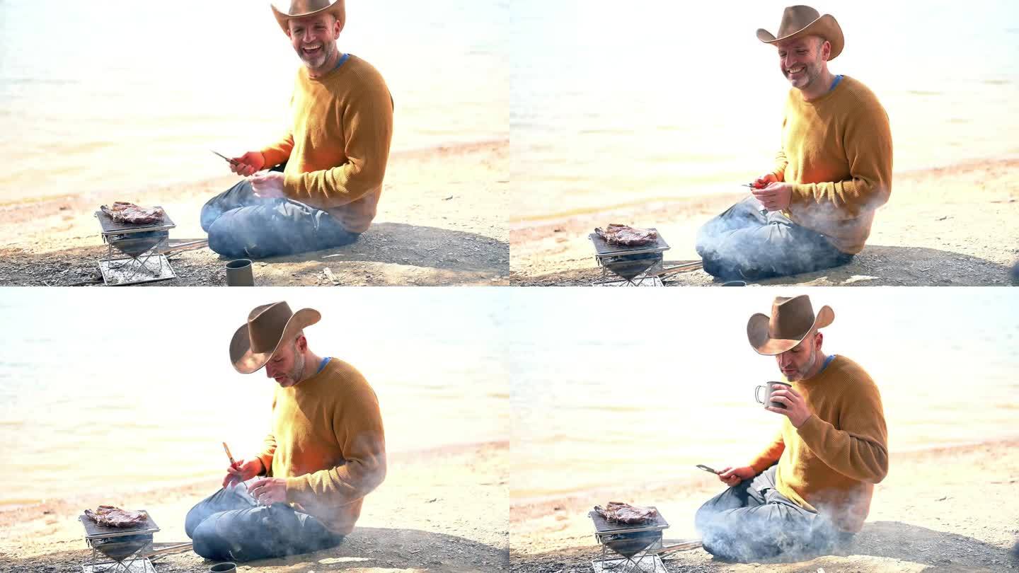 准备烤肉串的年轻人把肉片放在烤肉串上，坐在篝火旁的海石沙滩上