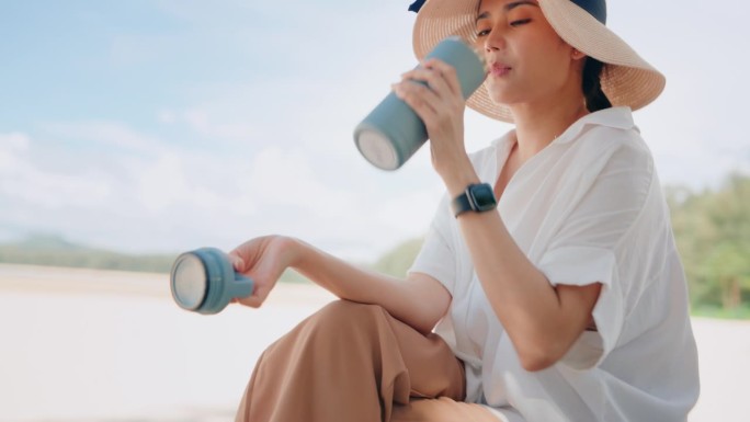 零浪费绿洲:海滩旁的女人用可重复使用的杯子喝水