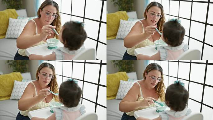 母女俩在一起，热爱家庭生活方式，在宝宝吃午饭的时候，随意地坐在家里，拿着勺子和围兜，专心地在客厅里吃