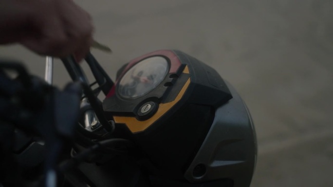 摩托车手将钥匙插入摩托车的点火装置并转动它来启动马达。头灯打开。带有速度计的摩托车仪表盘。男子启动摩