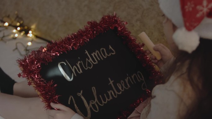 一个小女孩举着黑板，上面写着“圣诞节志愿服务”。圣诞志愿概念。