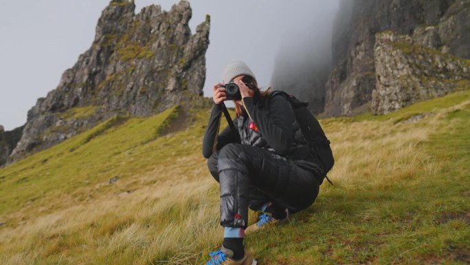 徒步登山的女人。坐在草地上，用相机拍照