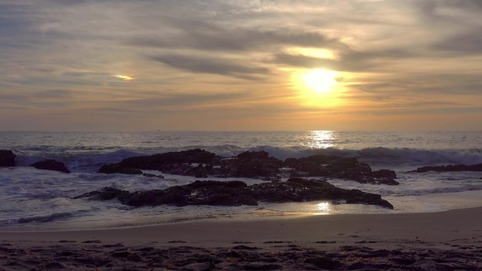 在4k的金色日落中，拉古纳海滩上的海浪撞击着岩石