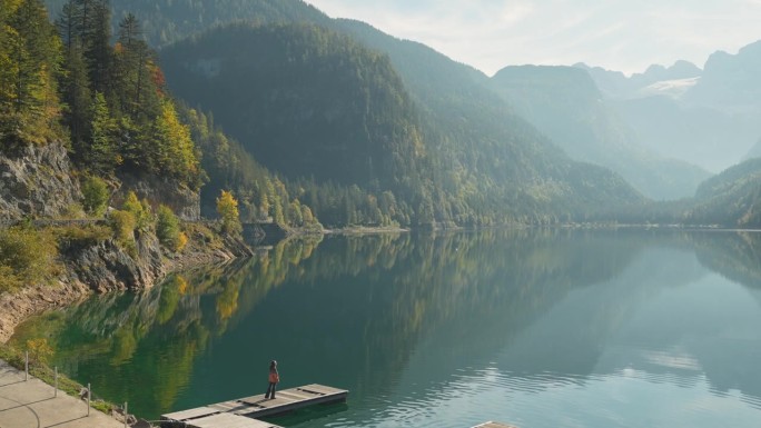 一个女人站在湖边的码头上，看着岣梢湖和山脉的景色