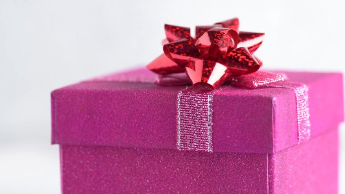 闪闪发光的粉红色礼盒与一个红色的蝴蝶结旋转。生日派对或圣诞节的概念。粉色礼品盒，近一点