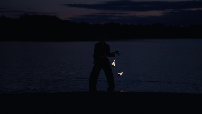 女子在夜晚的湖岸杂耍燃烧的火把的剪影，慢动作电影镜头