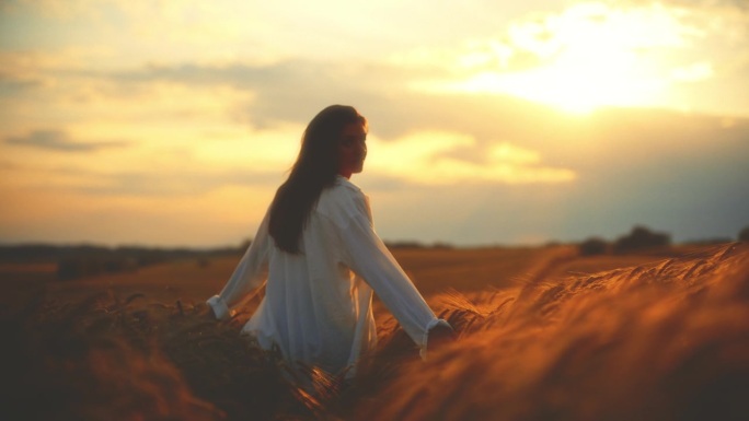 年轻女子漫步在农场的庄稼间，欣赏夕阳