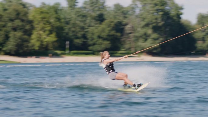 女子滑水板。女孩骑在滑水索上。握住牵引绳。夏天在湖里活动。以50fps录制。