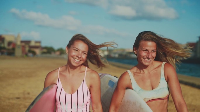 快乐的女性冲浪朋友们在阳光明媚的海滩上带着冲浪板散步