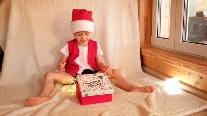 穿着圣诞老人服装的小男孩打开装有黑兔子的礼盒，高兴极了。童年与宠物的爱。圣诞快乐。兔是中国农历202