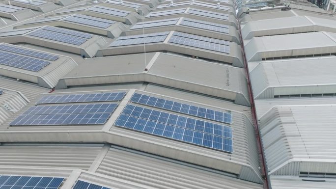 电力制造业厂房屋顶上许多太阳能电池屋顶农场的高角度面视图或无人机视图。