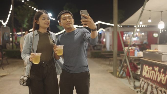 幸福的亚洲情侣用智能手机自拍在户外庆祝圣诞夜和新年，新年假期和假期。年轻人一起庆祝，享受。