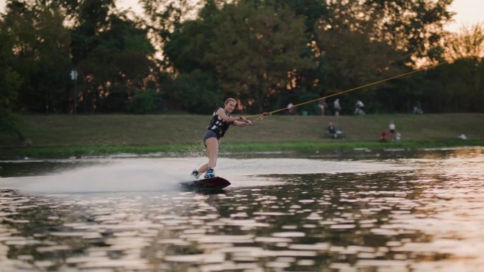 日落时分的女子滑水板运动员。女孩骑在滑水索上。握住牵引绳。夏天在湖里活动。120fps电影摄影机。