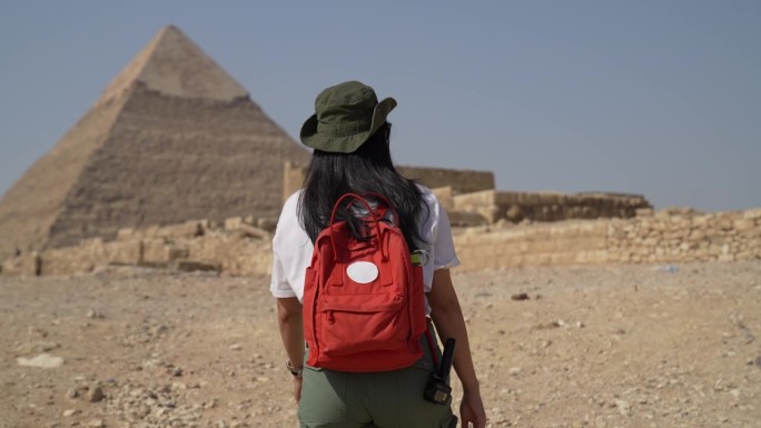 亚洲旅行者女子在吉萨金字塔背景的沙漠上行走