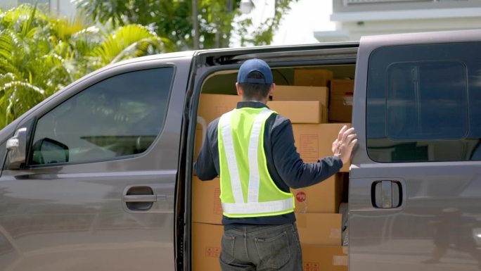 快递员从一辆货车上拿出盒子包裹，然后去房子里把包裹送到房主那里