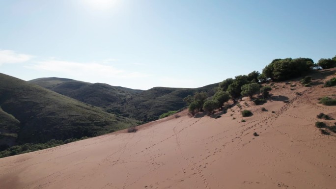 航拍摄影在倾斜的沙丘上，身后是长满草的山边，脚步声穿过景观