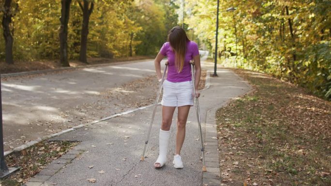 腿上打了石膏的女人在公园里走着用手机