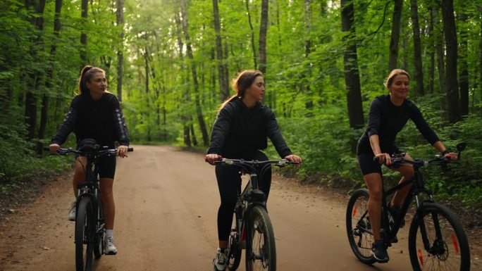 三个快乐的女人在大自然骑自行车，一群女运动员在森林里骑自行车