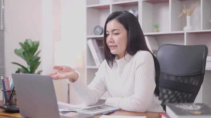 压力大的亚洲女性带着电脑在家里的客厅里工作