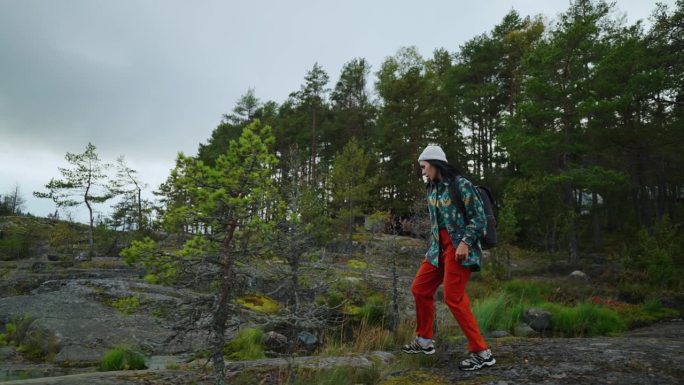 在挪威背包旅行，年轻的女旅行者走在美丽的松林附近的大石头上