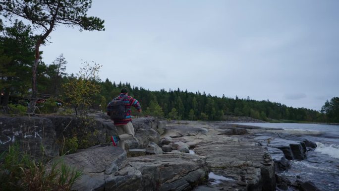 在挪威徒步旅行，游客背着背包独自走在松树林附近美丽的湖边