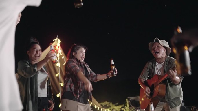 一群朋友弹着吉他，喝着啤酒，在剪影夕阳的背景下，美丽的自然，高山和湖泊，友谊和庆祝的概念。