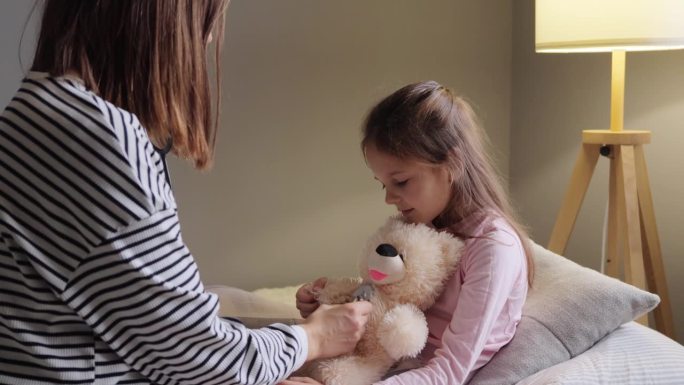 妈妈和小女儿在家里扮演医生，孩子请病假，用听诊器听泰迪熊的声音，孩子感冒了，玩得开心。