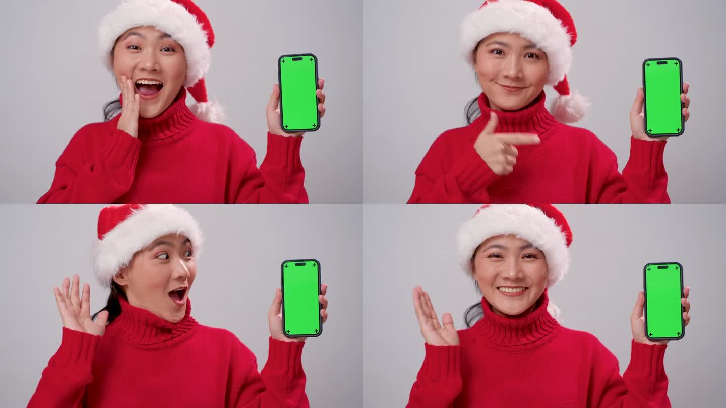 亚洲妇女戴着圣诞老人的帽子，开心地微笑着，拿着智能手机，显示绿色屏幕，孤立在白色背景上。