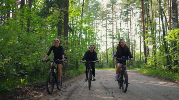 在森林里度过快乐的周末，三个年轻的女人在美丽的夏日里骑自行车