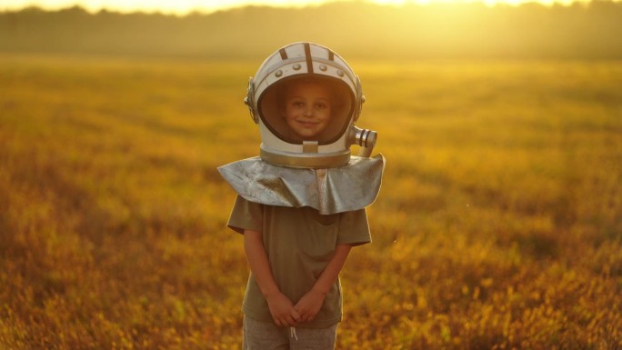 可爱的小宇航员男孩看着相机微笑的肖像，戴着太空头盔的孩子在野外