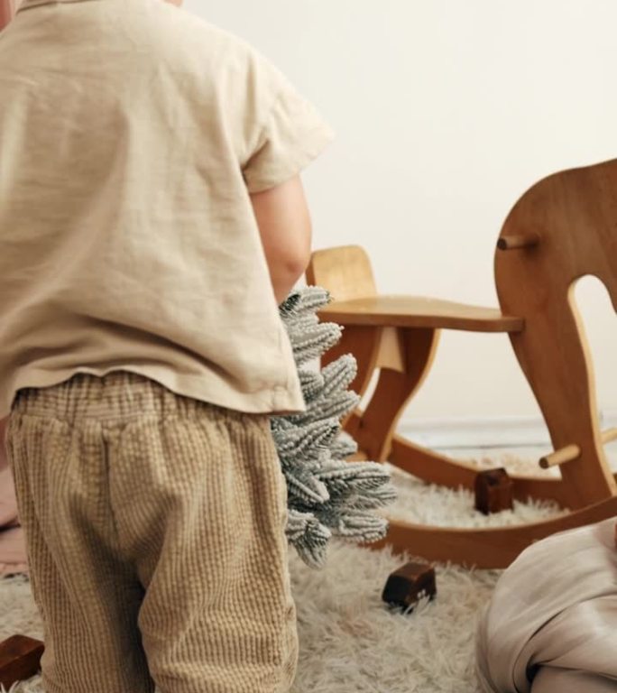 一个小男孩和他的妈妈在房间里装饰一棵小圣诞树，背景是一个玩具木马。垂直视频