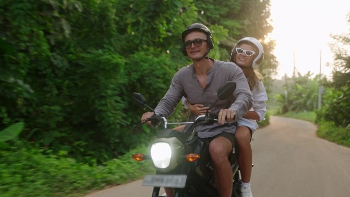 一对恋人骑着摩托车在丛林中旅行。一对幸福的夫妇在热带的夕阳下骑着摩托车。女友，男友开滑板车。游客享受