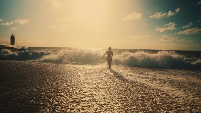 无忧无虑的年轻女子从海滩奔向阳光明媚的海浪