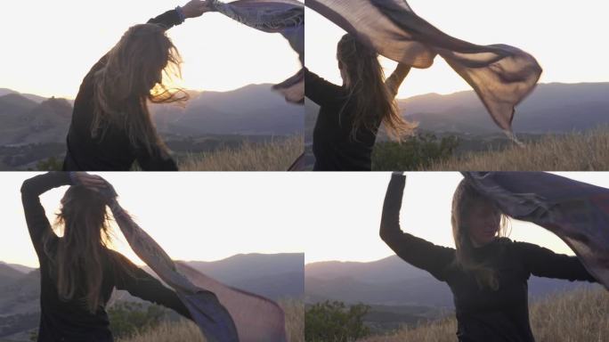 一名身穿黑色衣服的女子在山景的背景下，戴着围巾微笑着跳舞。一种心理状态的象征性拟人化。心理学和保健