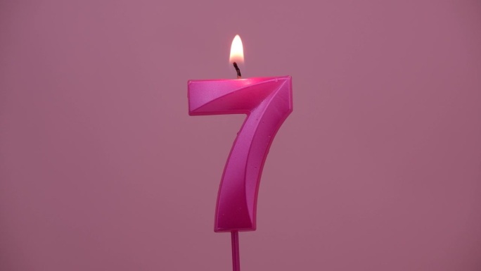 燃烧的生日蜡烛在粉红色的背景，7号。