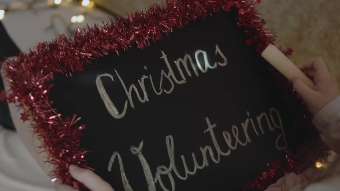 一个小女孩举着黑板，上面写着“圣诞节志愿服务”。圣诞志愿概念。Slowmotion