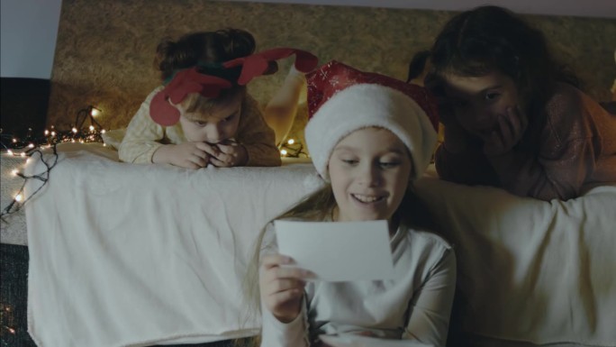 三个小女孩在圣诞夜一起看旧照片。到处都是圣诞彩灯。圣诞节和亲密的概念。