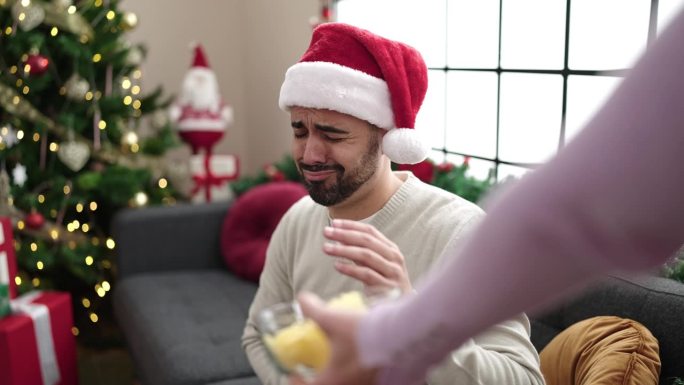 一名年轻的西班牙裔男子因头痛和胃痛坐在家里的圣诞树旁