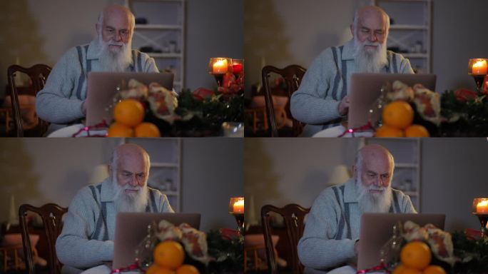 烛光下，一位大胡子老人坐在一张喜庆的桌子旁，摆弄着一台笔记本电脑。
