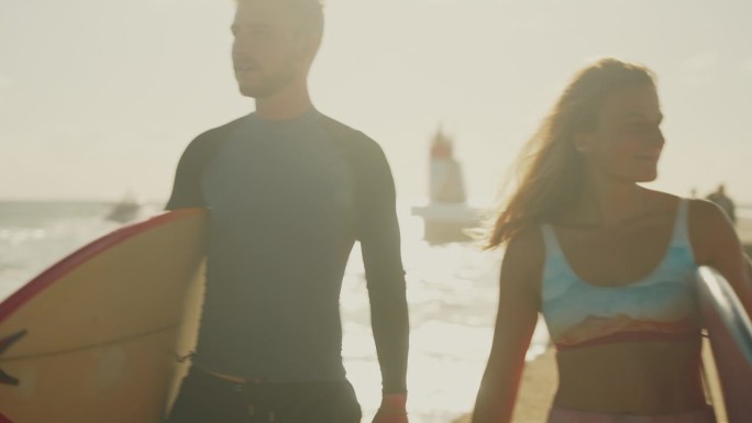 一对冲浪夫妇拿着冲浪板在阳光明媚的海滩上散步