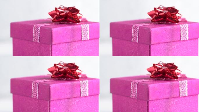 闪闪发光的粉红色礼盒与一个红色的蝴蝶结旋转。生日派对或圣诞节的概念。粉色礼品盒，近一点
