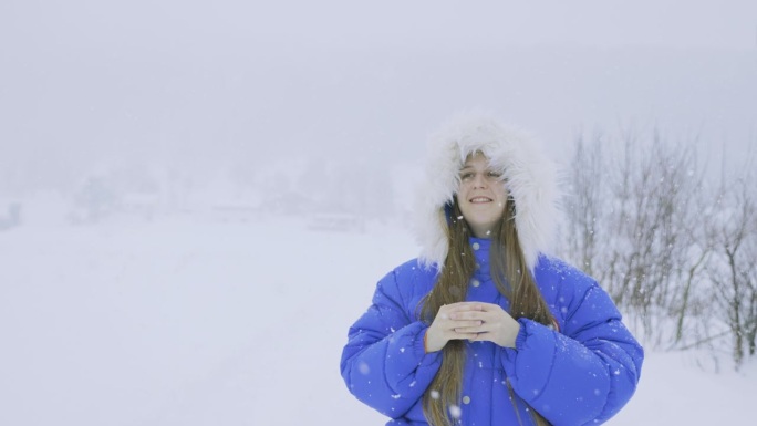 穿着蓝色外套的女人欣赏真正的冬季童话，在大雪中漫步在斯堪的纳维亚村庄