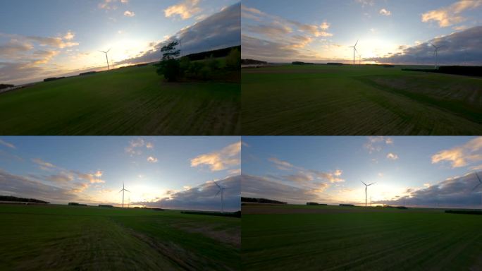 FPV竞赛无人机飞向风力涡轮机。夕阳下的波兰，风力涡轮机创造出可再生的绿色能源。