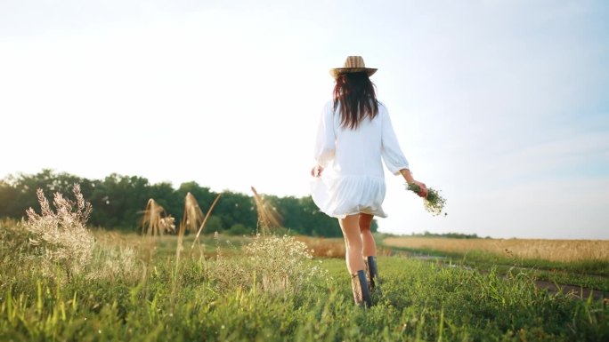 后视图年轻女子跑过洋甘菊田在美丽的夏装，在她的手捧一束新收集的野生雏菊。享受夏日和户外的大自然。