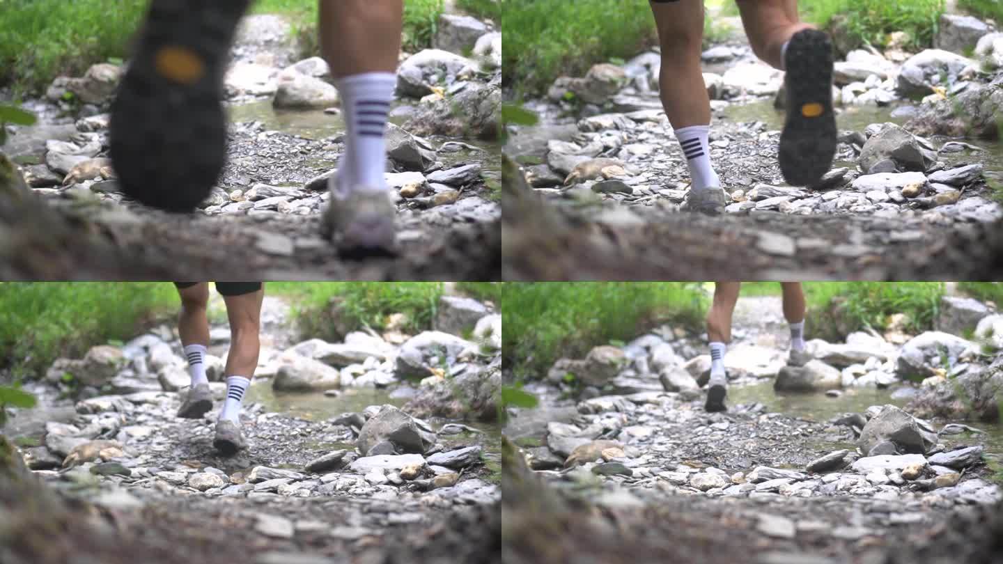徒步旅行的人的腿沿着岩石小路前进，跳过一条小河。穿着白袜子的年轻敏捷的徒步旅行者。