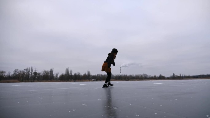 一个小女孩在多云的冬日里在结冰的河流上滑冰。穿着花样滑冰鞋的女滑冰运动员在室外溜冰场上滑行。女运动员
